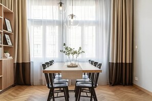A dining area with a wooden table, black chairs, a vase with plants, and a bookshelf. - Chic Two-Bedroom Residence in Vinohrady (Praha 2)