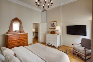 Een slaapkamer met een groot bed, een houten dressoir, een witte kast, een stoel, een televisie en een kroonluchter.