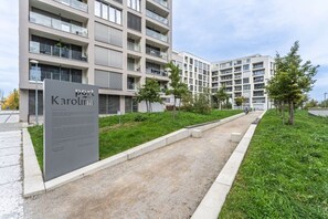 Ein modernes Mehrstöckgebäude mit begrüntem Bereich und Bäumen sowie einem Schild.