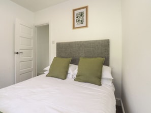 A neatly made bed with a grey headboard, two green pillows, and white bedding. - Beacon Fell Cottage 1 (Preston)