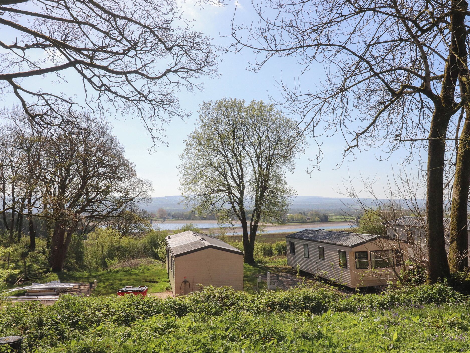 Een landelijk landschap met een klein huis, een schuur en een rivier op de achtergrond.