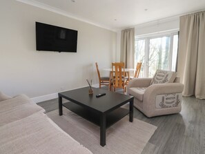 A living room with a flat-screen TV, a coffee table, a sofa, and a dining area with chairs and a table. - Beacon Fell Cottage 1 (Preston)