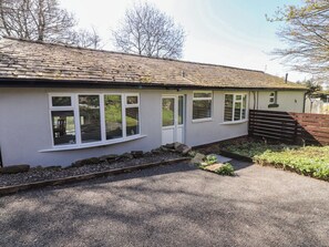 A single-story building with a sloped roof, multiple windows, and a gravel driveway. - Beacon Fell Cottage 1 (Preston)