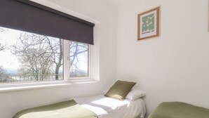 Ein Zimmer mit einem Bett, zwei Nachttischen, einem Fenster mit Ausblick und einem gerahmten Bild an der Wand.