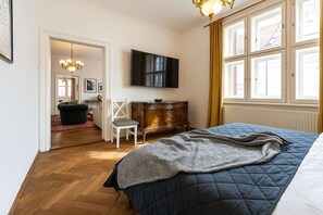 Ein Schlafzimmer mit einem Bett, einem Fernseher, einer Holzkommode, einem Sessel und einem Fenster mit Vorhängen.