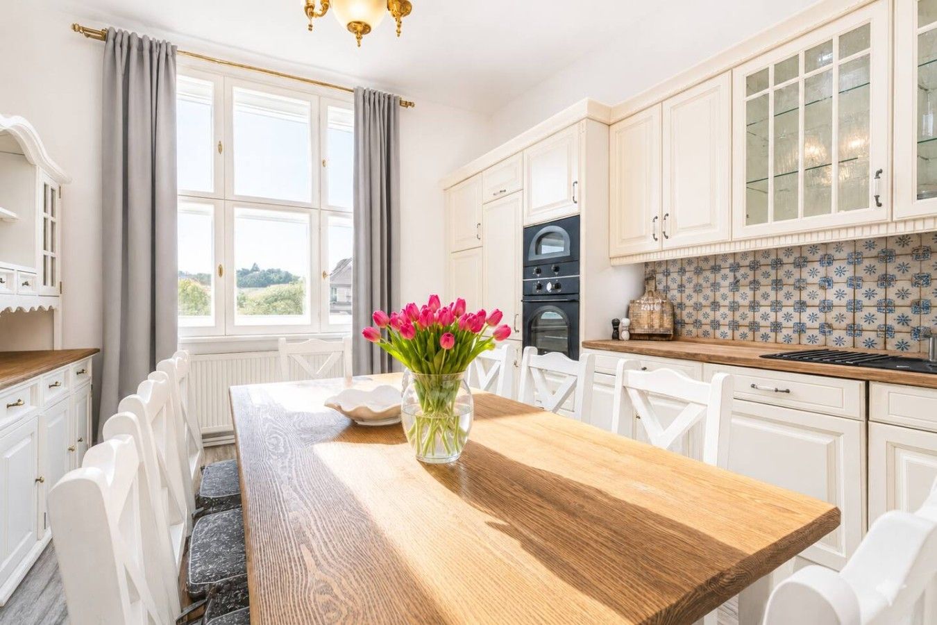 Una cocina moderna con armarios blancos, una mesa de comedor de madera y un jarrón de tulipanes.