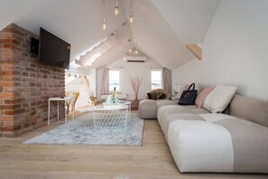 A modern loft with exposed brick, a white sofa, a round coffee table, and a TV mounted on the wall. - Old Town 2-BR Loft with Panoramic Prague Castle Views (Praha 1)