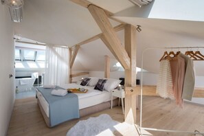 A bedroom with a skylight, wooden beams, a bed with pillows, a bedside table, and a clothing rack. - Old Town 2-BR Loft with Panoramic Prague Castle Views (Praha 1)