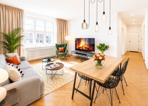 A modern living room with a sofa, a dining table with chairs, a fireplace, and hanging light fixtures. - Modern apartment in the heart of the Old Town (Praha 1)