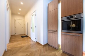 Ein Flur mit Holzboden, einer Tür mit geometrischem Muster und einer Küchenzeile mit Holzschränken und einem eingebauten Ofen.