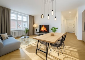 Ein modernes Wohnzimmer mit Sofa, Fernseher, Esstisch, Stühlen und Kamin.