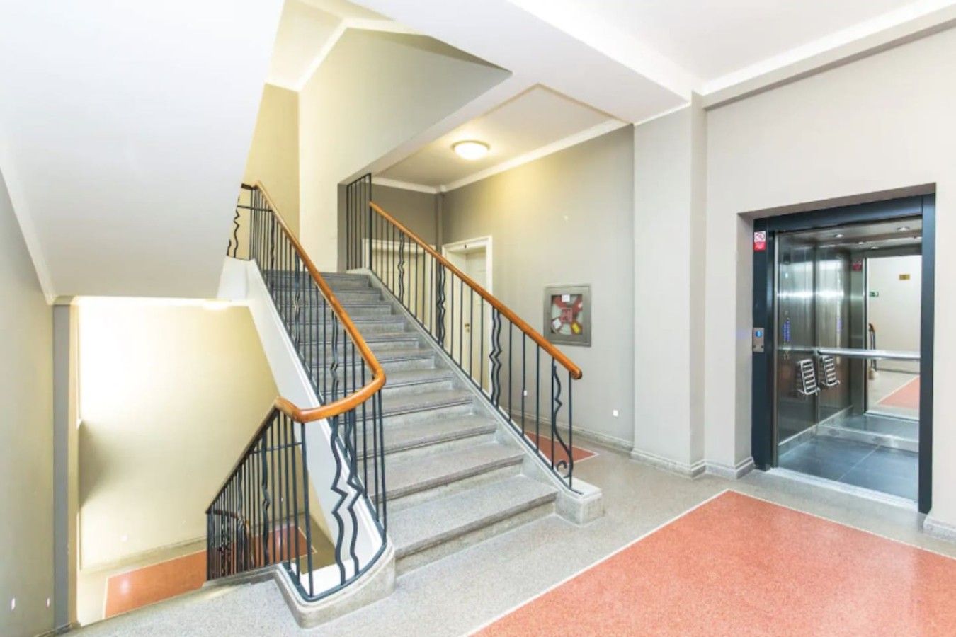 Un escalier doté d’une main courante et de rampes métalliques, menant à un ascenseur.