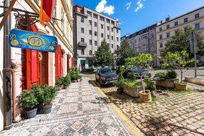 Eine Kopfsteinpflasterstraße mit einem Gebäude, das ein blaues Schild mit goldener Schrift, Blumentöpfen und abgestellten Autos zeigt.
