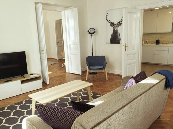 Un salon comprenant un canapé, une table basse, un téléviseur, un fauteuil et un tableau représentant un cerf accroché au mur.
