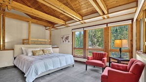 Quarto com cama, duas cadeiras, luminária e janelas amplas.