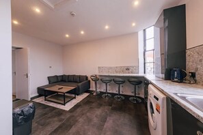 A modern kitchen with a built-in washing machine, a bar stool area, and a seating area with a sofa and coffee table. - Modern Escape Apartment | Central Edinburgh (Edinburgh)