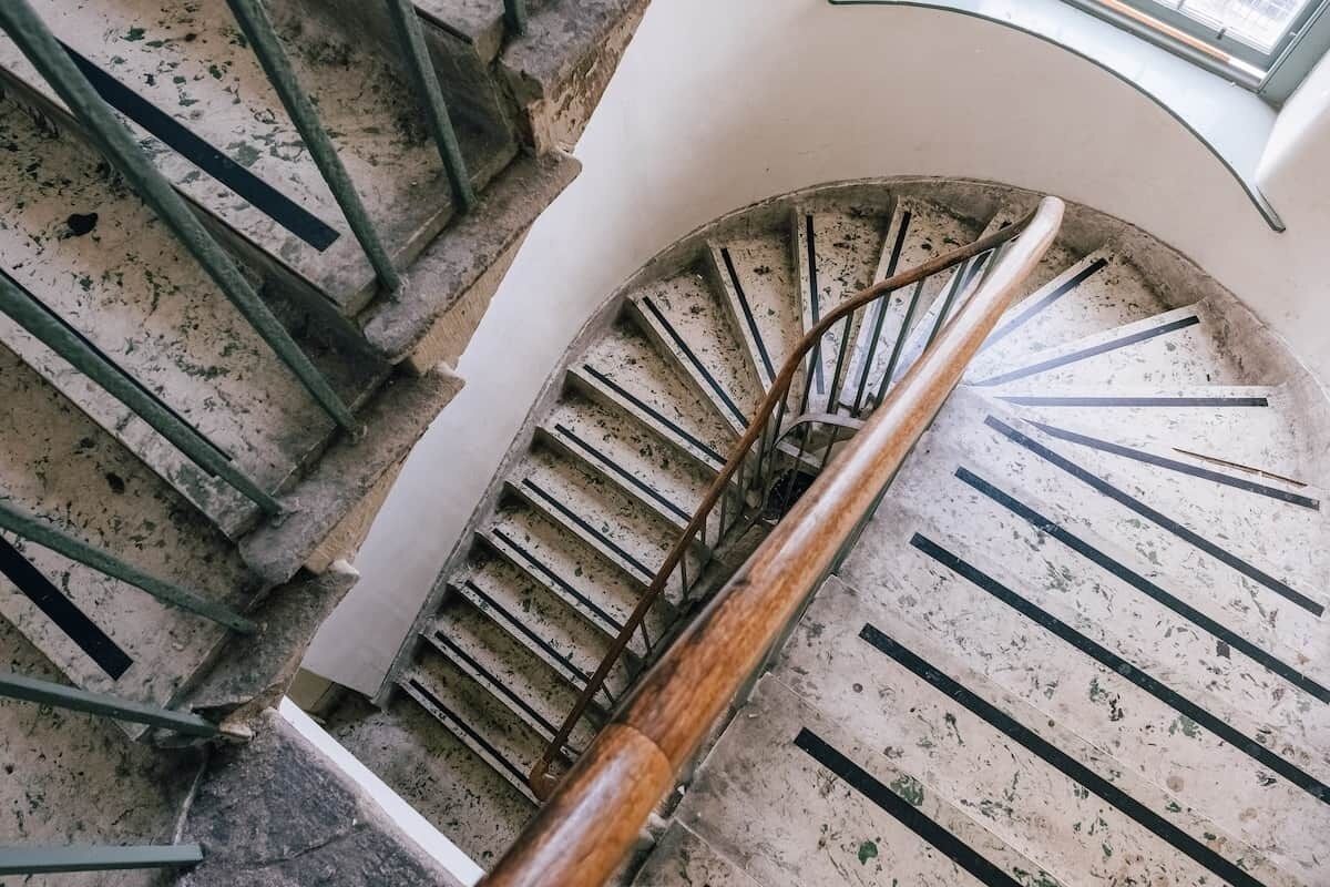 A spiral staircase with a wooden handrail and metal balusters, leading to an upper floor.