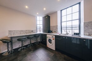 Una cocina moderna con lavadora, taburetes de bar y ventanas amplias.