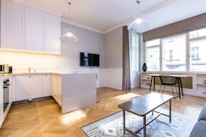 A modern kitchen with white cabinets, a central island, and a dining area with a table and chairs. - Luxury One-Bedroom Retreat in Old Town (Praha 1)