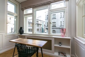 A room with a table, a chair, a radiator, and a window with a view of buildings. - Luxury One-Bedroom Retreat in Old Town (Praha 1)
