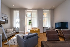 Ein modernes Wohnzimmer mit einer Couch, Sesseln, einem Fernseher und großen Fenstern.