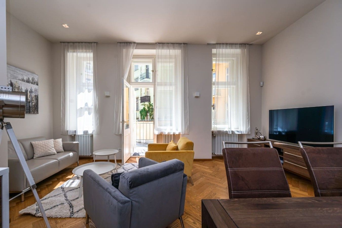 Een moderne woonkamer met een bank, stoelen, een televisie en een groot raam met gordijnen.