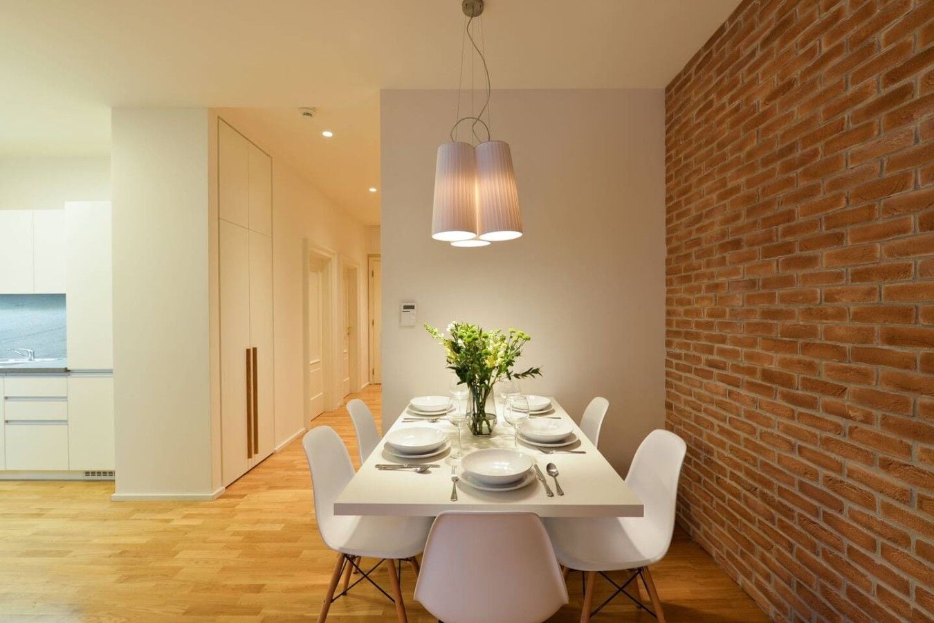 A dining area with a brick wall, white table, and chairs.