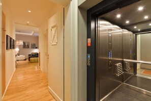Ein Flur, der zu einem Aufzug mit modernem Design führt, mit einer Couch und einem Couchtisch im Hintergrund.