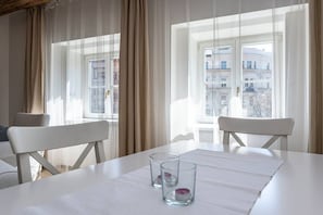 Ein Hotelzimmer mit großem Fenster, zwei weißen Stühlen, einem weißen Tisch und zwei klaren Gläsern mit Kerzen.