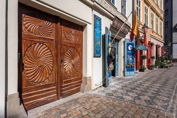 Eine Straße mit Kopfsteinpflaster, eine Holztür mit aufwendigen Schnitzereien und ein Gebäude mit einem blauen Schild, auf dem 'MUSEUM' steht.