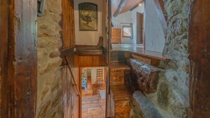 Un interior rústico con paredes de piedra, vigas de madera, una escalera y un banco.