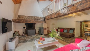 Una sala de estar acogedora con chimenea de piedra, una mesa de centro blanca, un sofá rojo y techo de madera.