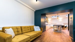 A modern living room with a yellow sofa, a dining area with a table and chairs, and a kitchen visible through an open door. - Designer Two-Bedroom Loft with Terrace in Old Town (Praha 1)