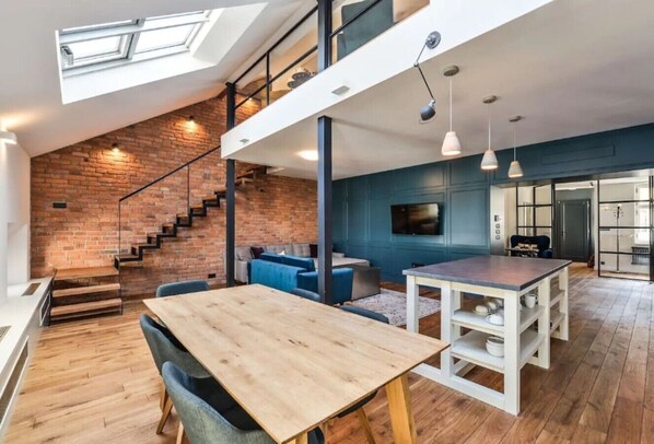 Ein Loft-Zimmer mit Esstisch aus Holz, einer Treppe und einer Wand in Blautönen.