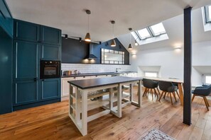 Eine moderne Küche mit dunkelblauen Schränken, einer zentralen Kochinsel und einem Essbereich mit hoher Decke und Dachfenstern.