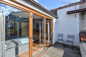 Ein Wohnraum mit einer Schiebeglastür, die auf einen Balkon führt, einer kleinen Außenbereich-Sitzgelegenheit mit zwei Stühlen und einer sichtbaren Treppe.