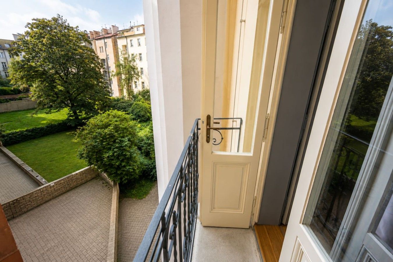 A balcony with a view of a well-maintained garden and neighboring buildings.
