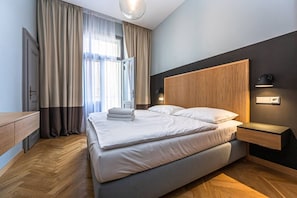 Ein modernes Hotelzimmer mit einem großen Bett, einem Holzkopfstück, Nachttischen und Blick ins Freie.