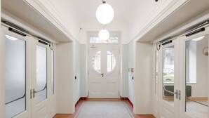 En hall med vita dörrar, en central, rund dörr och en mönstrad matta.