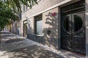 Ein Gebäude mit einem großen Fenster und einer Tür, eine Straße mit Kopfsteinpflaster und ein Baum, der Schatten wirft.