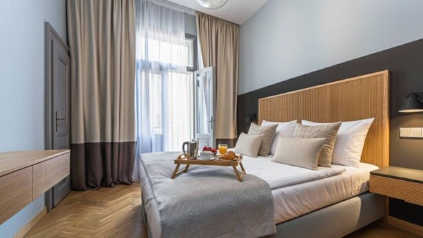 A modern hotel room with a large bed, wooden headboard, and a bedside table with a lamp. - Luxury Two-Bedroom Residence in Vinohrady (Praha 2)