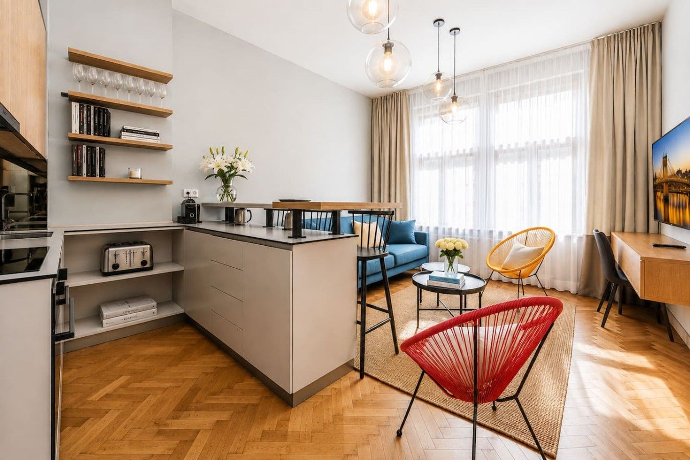 A modern kitchen with a central island, a dining area with a sofa and chairs, and a large window with curtains.
