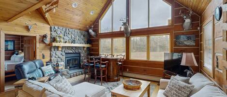 A cozy log cabin interior with a fireplace, wooden furniture, and deer antlers on the walls.
