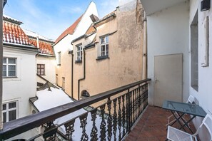 A balcony with a metal railing, a table, and chairs, overlooking a street with buildings. - Spacious Old Town Square Two-Bedroom Residence (Praha 1)