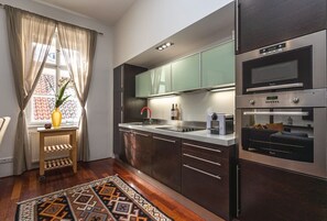 A modern kitchen with dark cabinets, stainless steel appliances, and a window with curtains. - Spacious Old Town Square Two-Bedroom Residence (Praha 1)