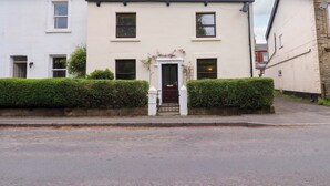 A two-story residential building with a white facade, a central entrance with a dark door, and a small garden area with a hedge. - 6 Hazel Moor (Blackburn)