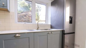 A kitchen with grey cabinets, a stainless steel refrigerator, a window, and a stone wall outside. - 6 Hazel Moor (Blackburn)
