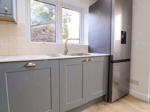 A kitchen with grey cabinets, a stainless steel refrigerator, a window, and a stone wall outside. - 6 Hazel Moor (Blackburn)