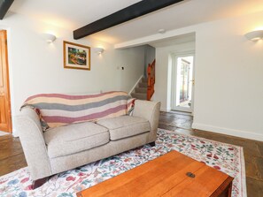 A living room with a sofa, a wooden coffee table, a floral rug, a staircase, and a door leading outside.