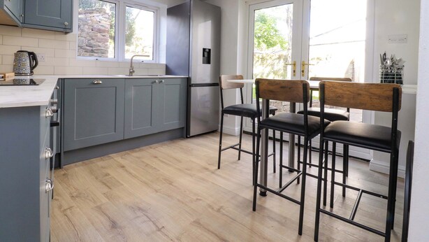 A modern kitchen with grey cabinets, a stainless steel refrigerator, and a dining area with two wooden chairs. - 6 Hazel Moor (Blackburn)